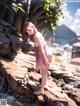 A woman in a pink dress standing on a rock by the water.