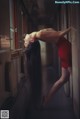 A woman in a red dress leaning against a window.