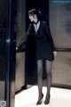 A woman in a black dress standing in front of a glass door.