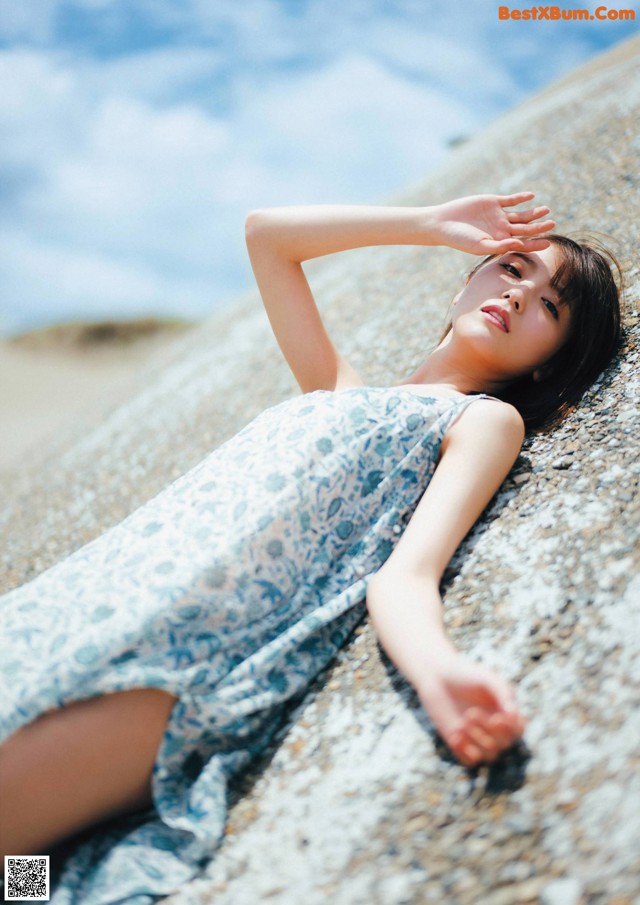 A woman laying on a rock on the beach.