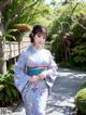 A woman in a blue kimono standing on a sidewalk.