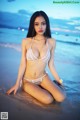 A woman in a white bikini sitting on the beach.