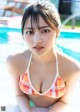 A woman in a bikini sitting by a swimming pool.