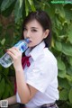 A woman in a school uniform drinking water from a bottle.