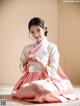 A woman in a pink and white hanbok sitting on the floor.