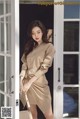 a woman standing in front of a door wearing a beige shirt dress