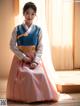 A woman in a pink and blue hanbok sitting on the floor.