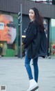 A woman in ripped jeans and a black shirt is walking down the street.