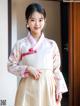 A woman wearing a white and pink hanbok standing in front of a door.