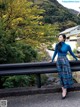 A woman in a blue turtle neck sweater and plaid skirt leaning against a railing.