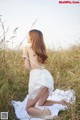 A woman in a white dress sitting in a field.