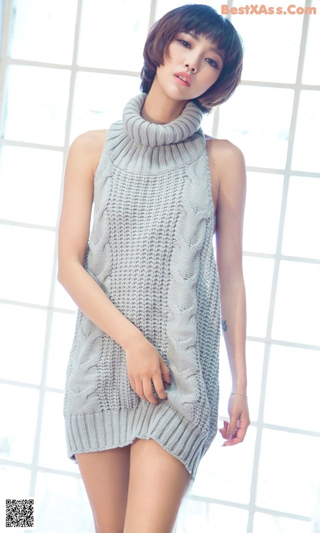 A woman in a gray sweater dress posing for a picture.