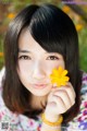 A woman holding a yellow flower in her hand.