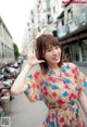 A woman in a floral dress waving at the camera.