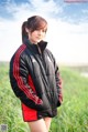 A woman in a black and red jacket standing in a field.