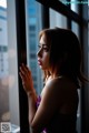 A woman in a purple dress looking out a window.